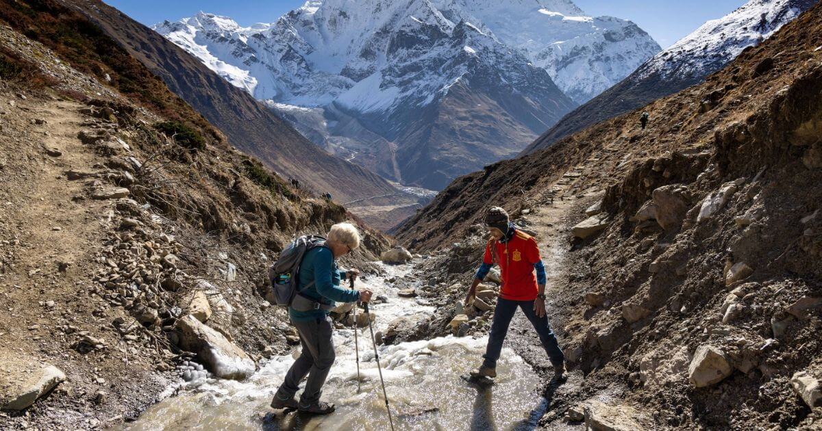 Guide helping trekker crossing a stream
